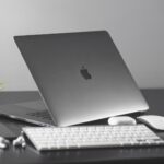 MacBook på skrivbord med tangentbord, mus och två gröna växter