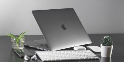 MacBook på skrivbord med tangentbord, mus och två gröna växter
