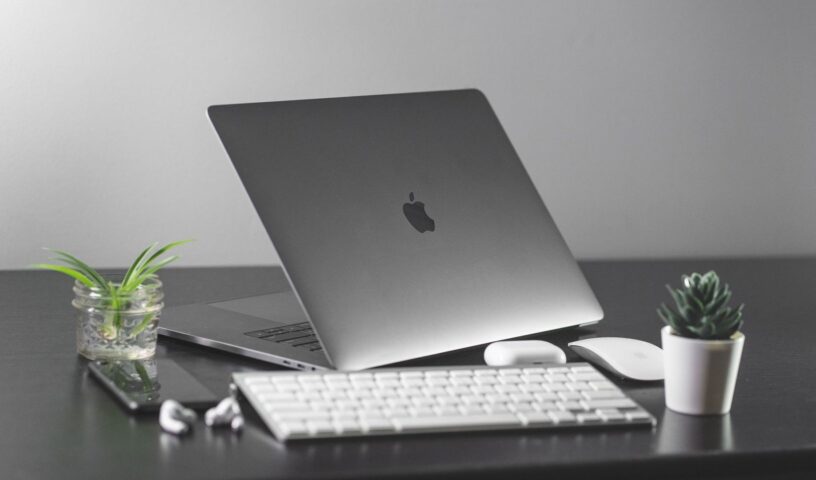 MacBook på skrivbord med tangentbord, mus och två gröna växter